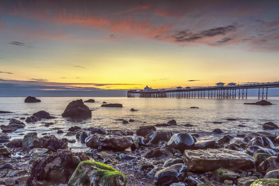 A picture of some rocks and the sea with a pier in the background