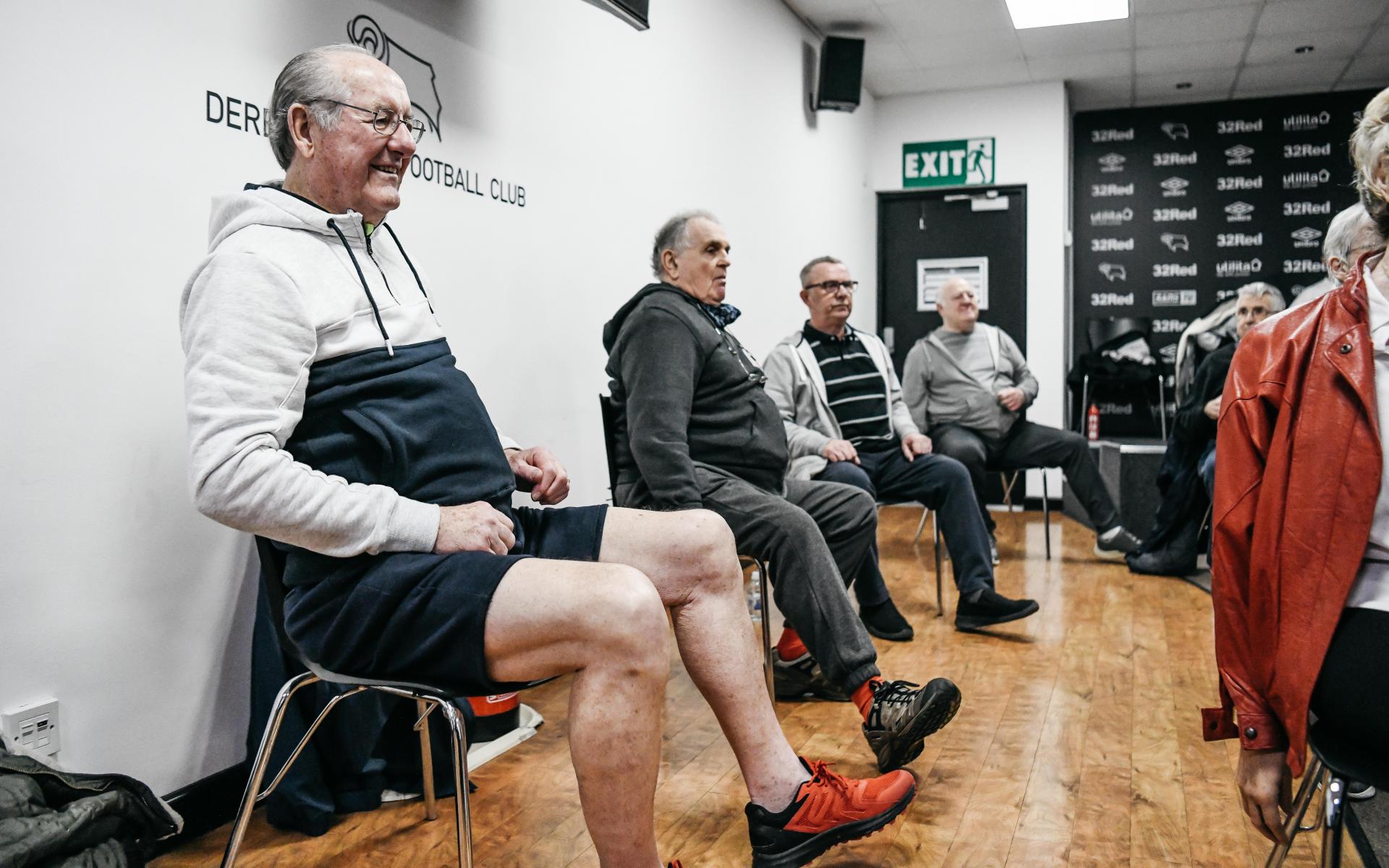 Men sitting on chairs smiling.