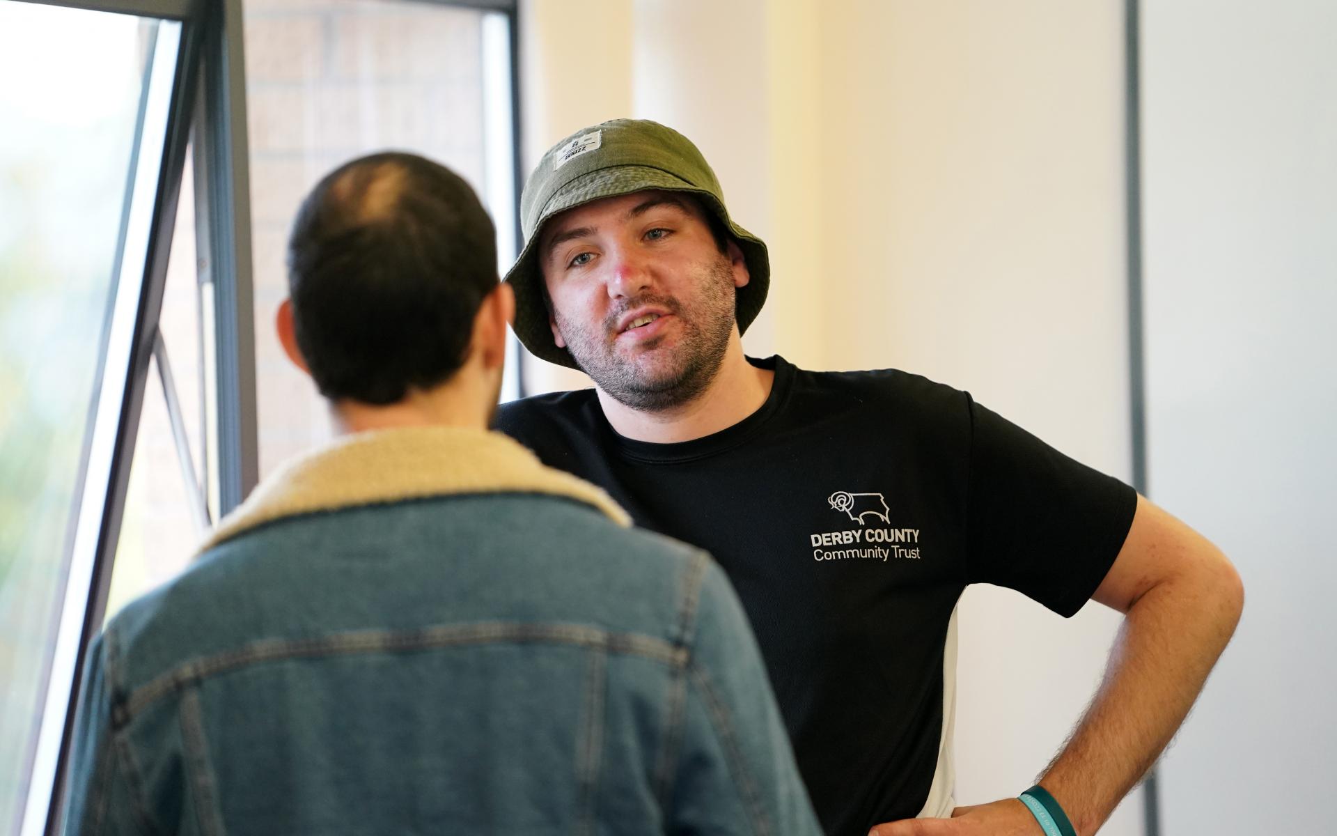 Two men talking, one wearing a hat.