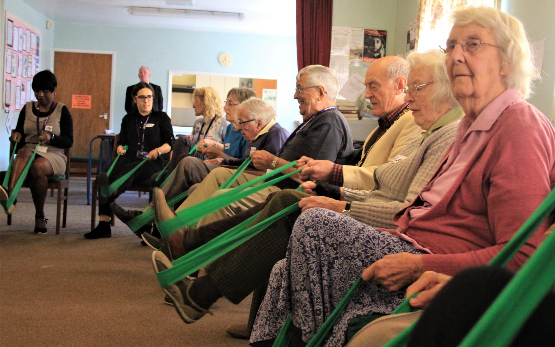 Elderly men and women sitting in chairs using resistance exercise bands.