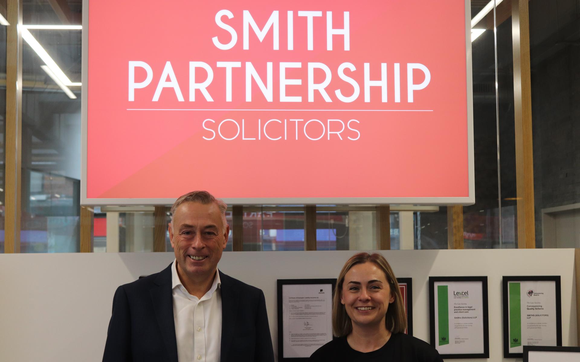 Smith Partnerships Managing Director with Emma Pilgrim, Events and Projects Manager at Derby County Community Trust, in front of the Smith Partnership logo