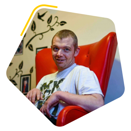 Male service user with Huntington's disease sat in a chair in bedroom