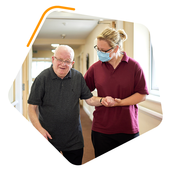 Care worker walking with male resident down care home corridoor