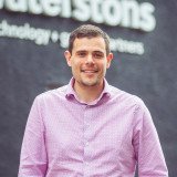 A white man with short, dark hair wearing a pink shirt