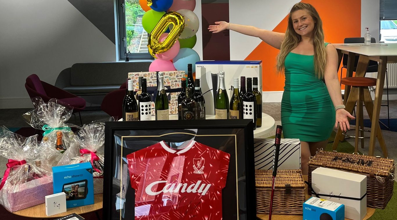 A young lady standing with a selection of items used as raffle prizes
