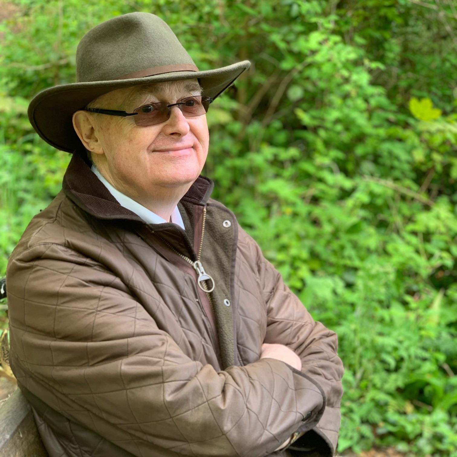 A man in a quilted jacket and green hat sitting on a bench