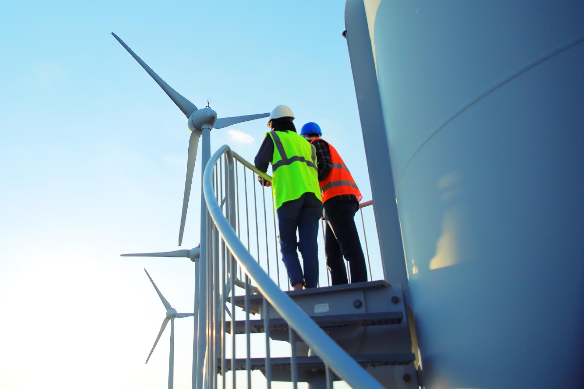 People in high-visibility tops standing next to a wind turbine, working on a renewable energy project