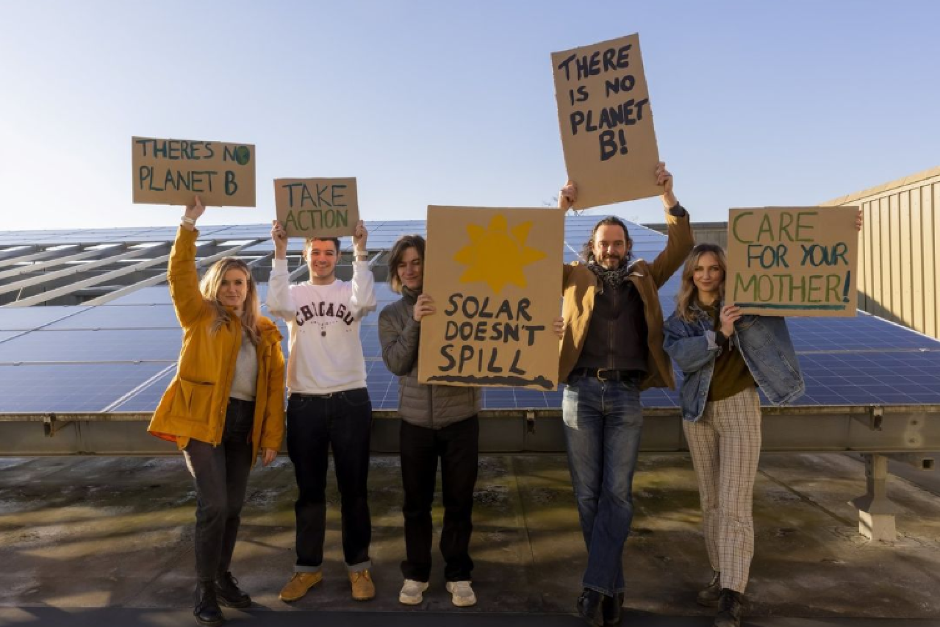 Colleagues standing in front of solar panels, holding a sign promoting climate action and sustainability