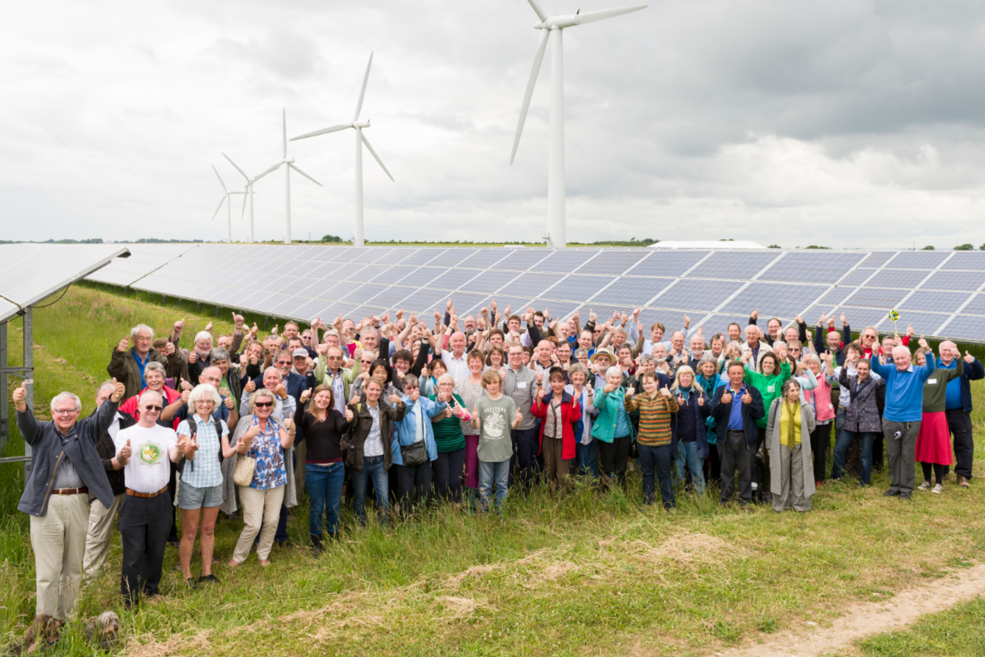 Shareholders standing in front of solar and wind farms, representing their involvement in a community energy project.