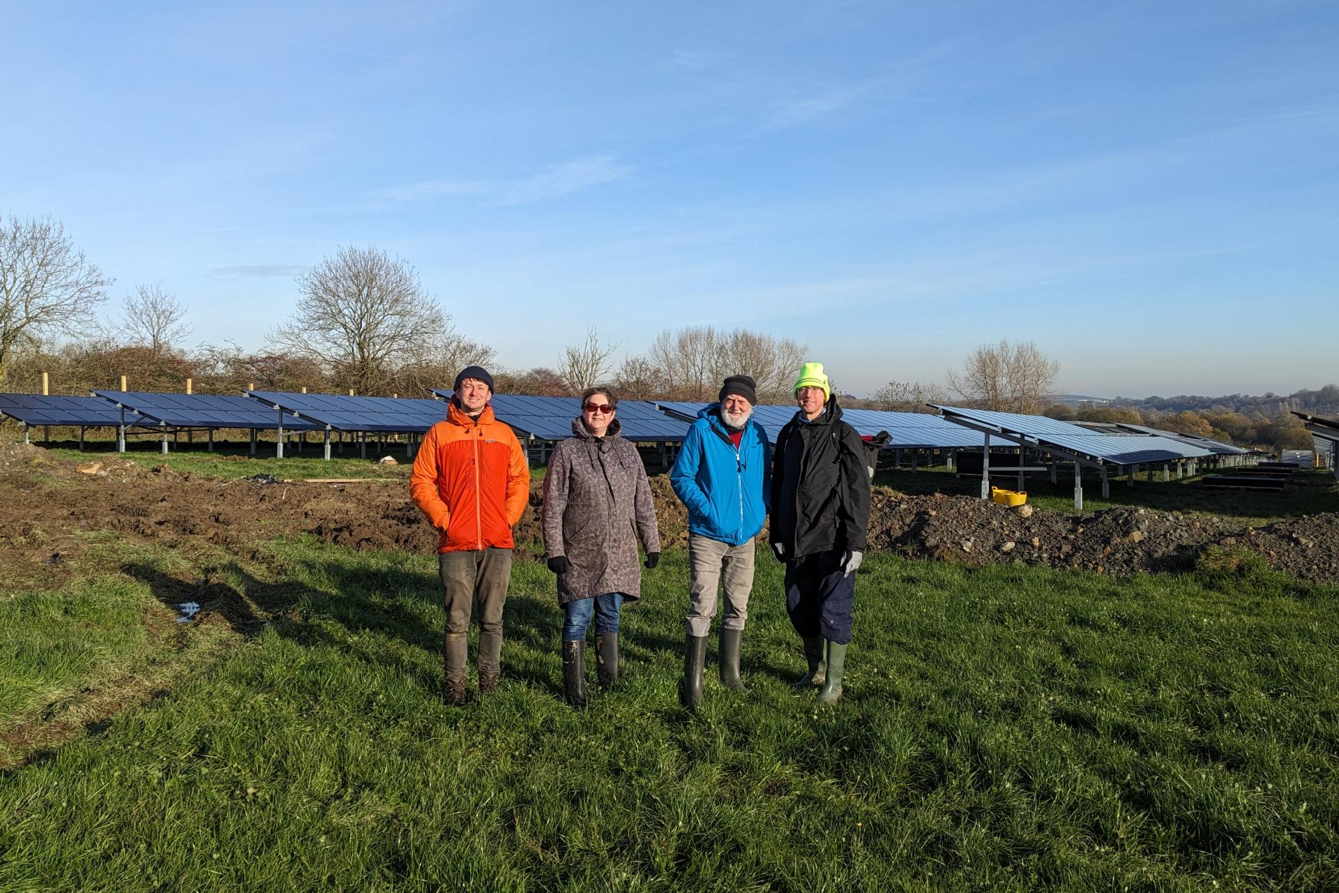 The Big Solar Co-op team standing in front of recycled solar panels at Whiteborough Solar Park.